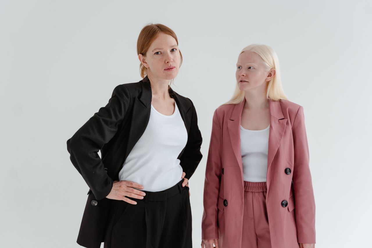 Services Two women in business suits exuding confidence on a white studio background.