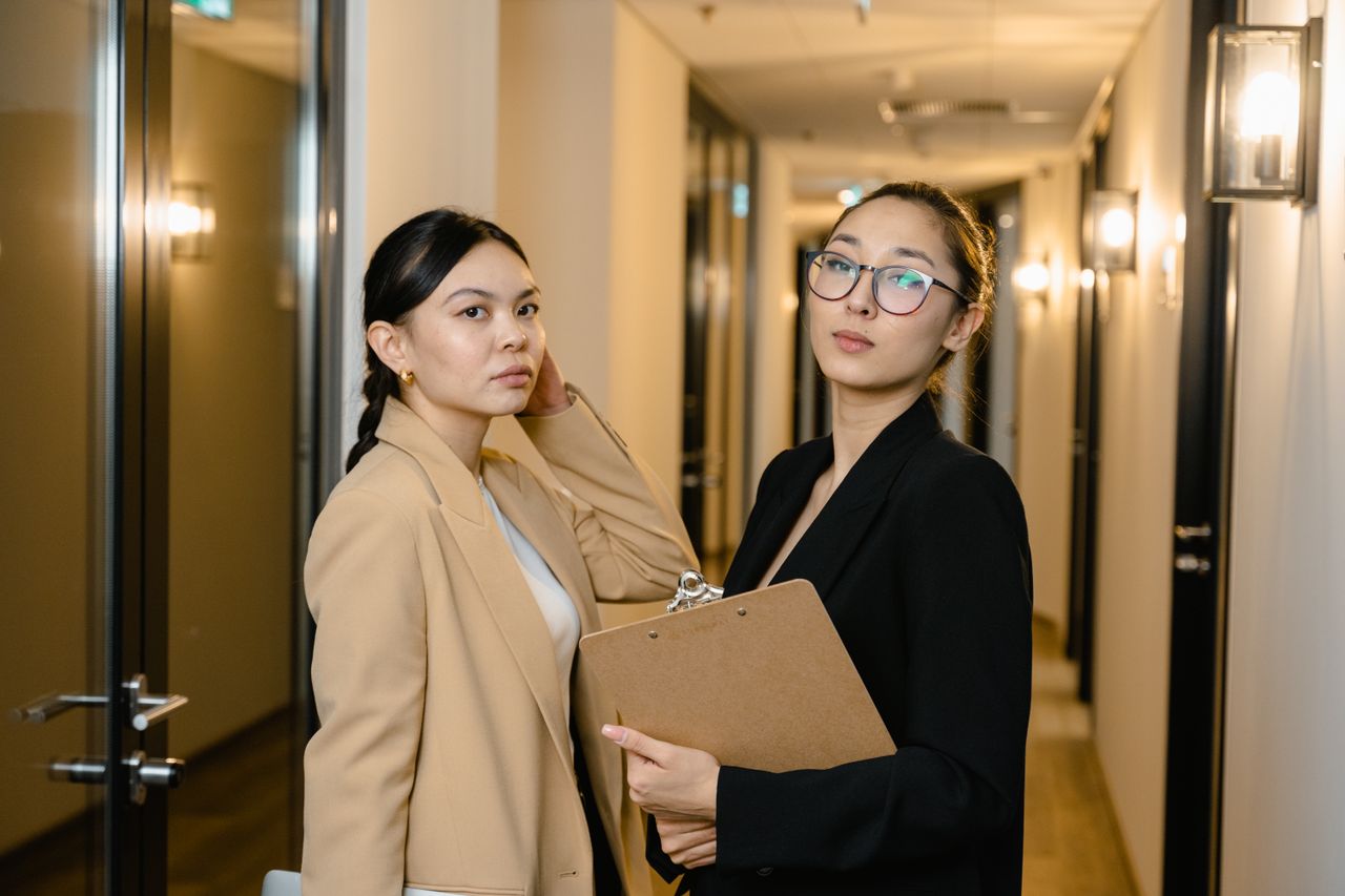 Home Two professional women in suits standing confidently in an office hallway.